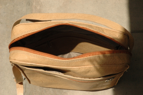 Tan leather bag with curved flap closure, open to reveal dark interior compartment, side view