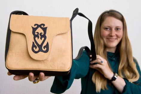 Woman holding tan leather shoulder bag with black geometric animal motif on front and adjustable black straps