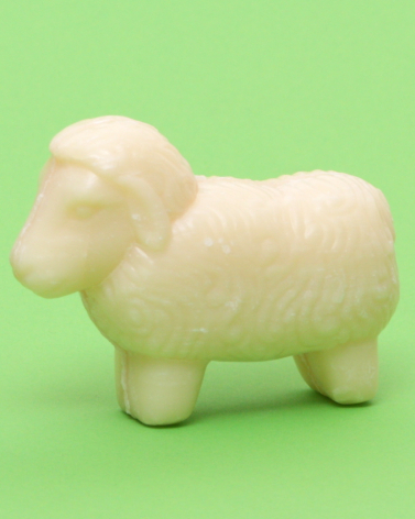 Cream-colored carved jade sheep figurine on bright green background, shown in side view