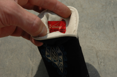 Hand holding open black leather pouch with red fabric interior detail, top view