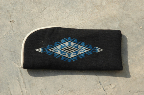 Black leather clutch with embroidered blue geometric diamond pattern on front, angled view