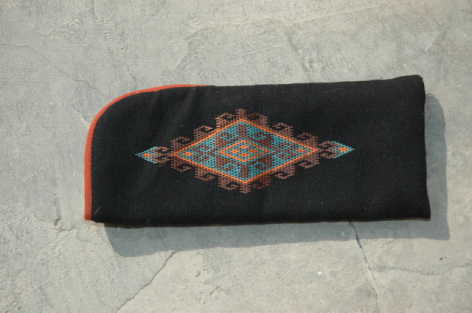 Black wool clutch with geometric orange and cream embroidered diamond pattern on front, orange edging visible on side