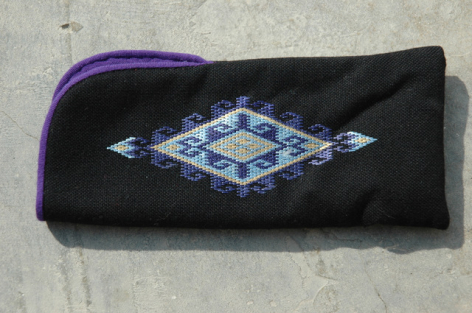 Black textile clutch with blue geometric diamond pattern and purple zip detail, front view