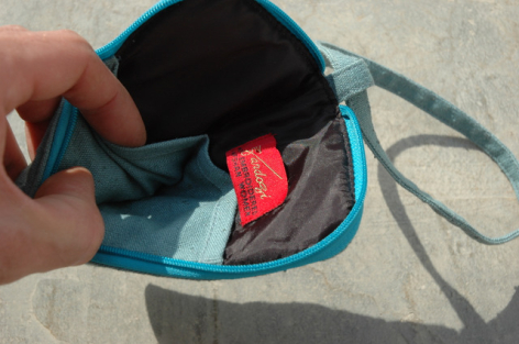 Teal leather pouch held open in hand, showing red fabric lining and interior compartment detail