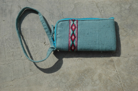 Petit portefeuille bleu turquoise en textile avec bandoulière noire et détail géométrique rouge et blanc