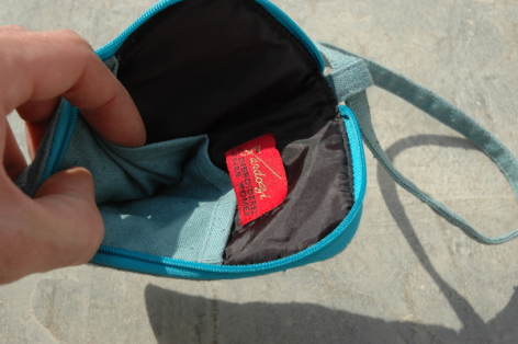 Petit sac en cuir bleu ouvert montrant sa doublure rouge et compartiment intérieur, tenu à la main