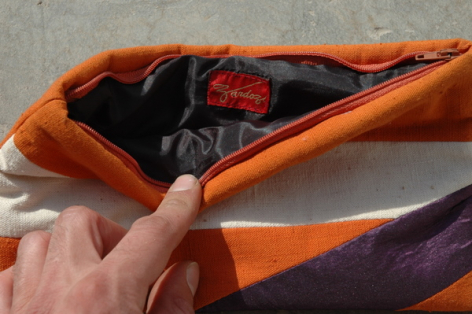 Sac en cuir orange vif ouvert montrant l'intérieur noir, tenu à la main en vue de détail