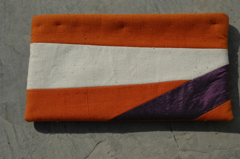 Rust, cream, and deep purple striped leather clutch with geometric color blocking detail, front view