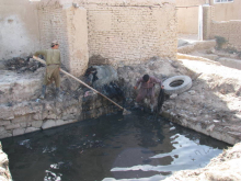 Artisan processing textiles in shallow water near brick structures, outdoor workshop with hands-on craftsmanship