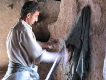 Handwerker bei der Verarbeitung von dunklem Textilstoff an einer Werkbank in traditioneller Werkstatt