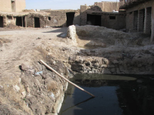 Canalisation d'eau à ciel ouvert traversant un village désertique aux bâtiments en pierre brute