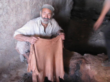 Handwerker hält braunes Textil ausgebreitet in den Händen, traditionelle Färbetechnik in Werkstatt